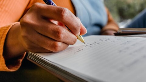 Großaufnahme einer Hand, die mit einem Kugelschreiber Notizen in ein Heft macht