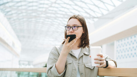 Female teenager in a school with cell phone and coffee cup in hand.