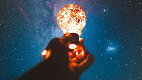 Hand holding a glowing light bulb up to the starry sky 