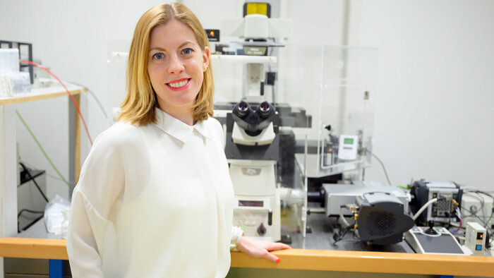 Junge Forscherin in weißer Bluse vor Mikroskop 